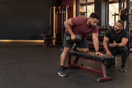 Coach guides a beginner through a dumbbell row in a gym